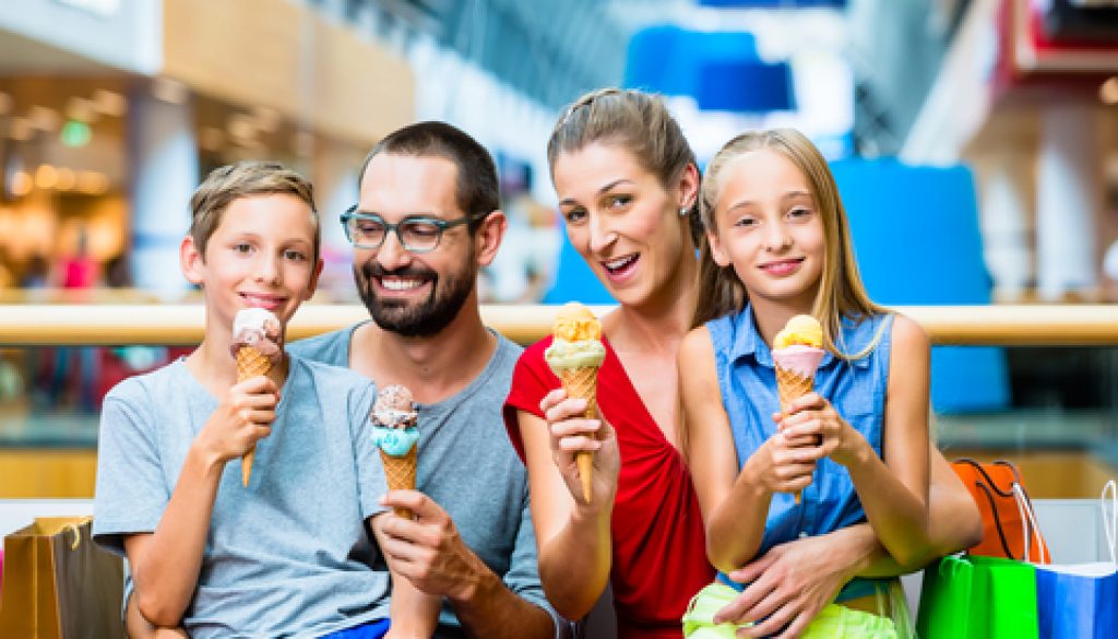 Family eating ice cream in shopping mall with bags